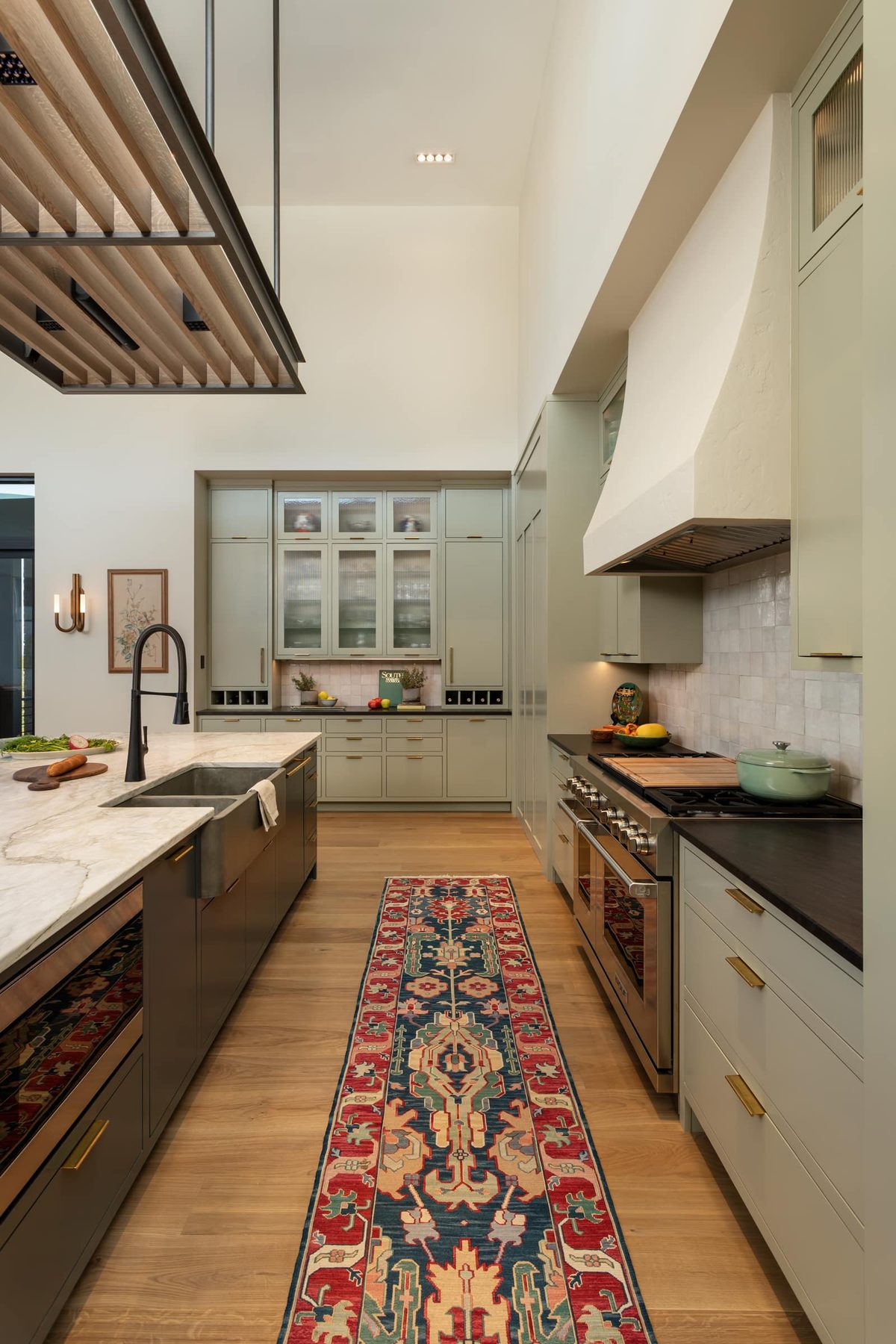 Galley view of the sage kitchen showing the range wall and a glass-front pantry wall
